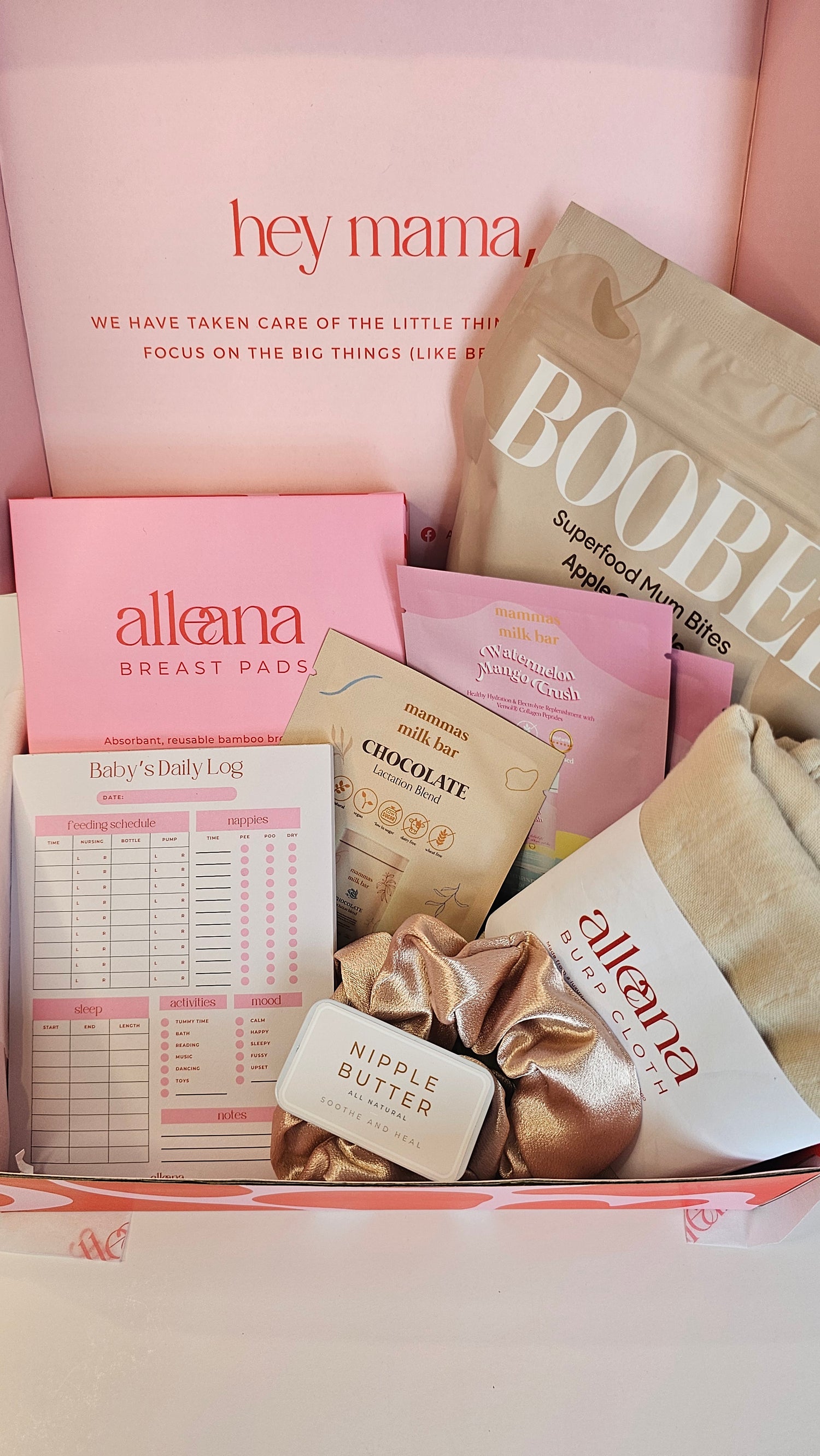 Flat lay of the Alle Ana breastfeeding bundle featuring breast pads, Boobee lactation bites, mama journal, nipple cream, and self-care items in pink and beige packaging.