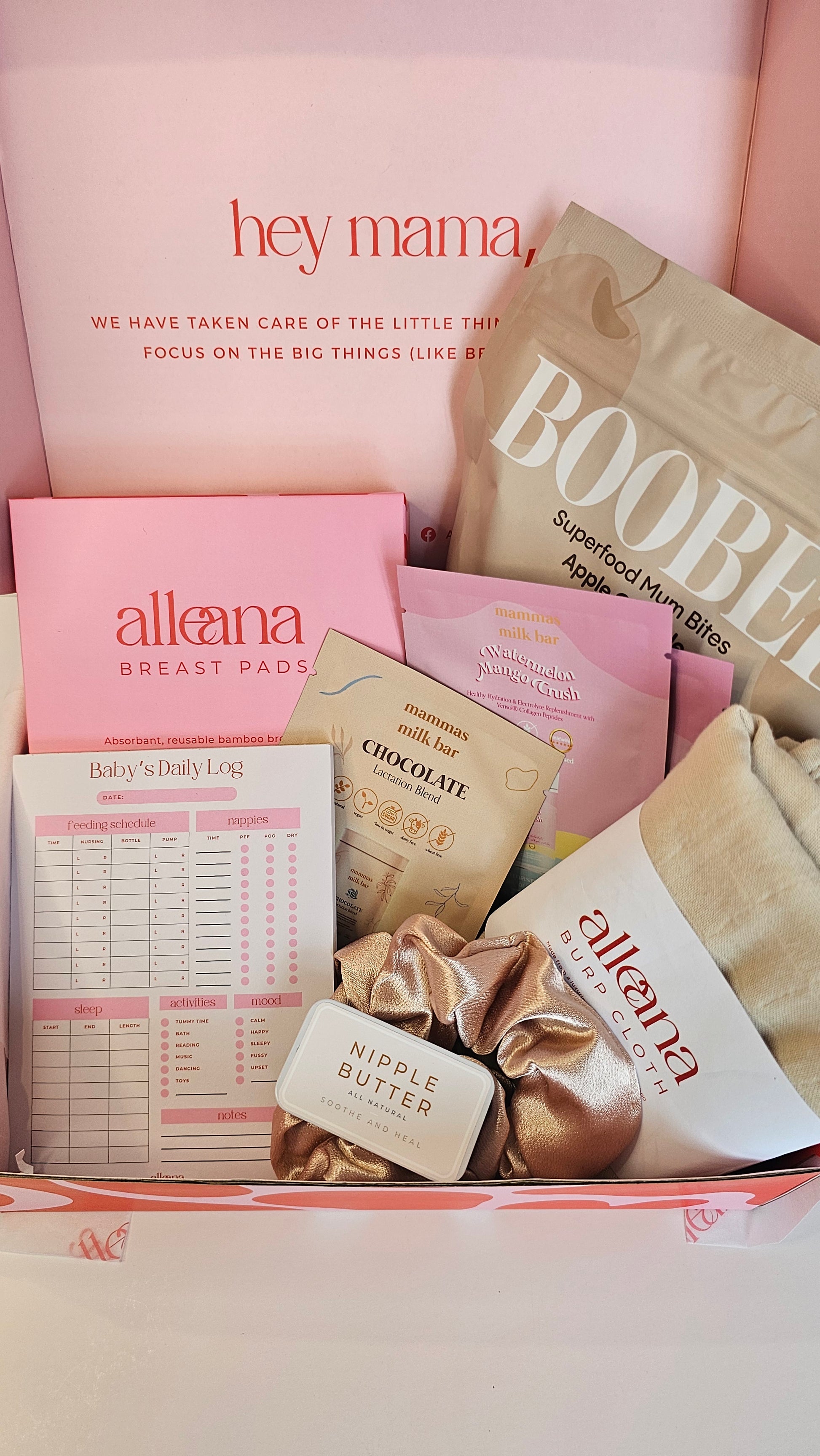 Flat lay of the Alle Ana breastfeeding bundle featuring breast pads, Boobee lactation bites, mama journal, nipple cream, and self-care items in pink and beige packaging.