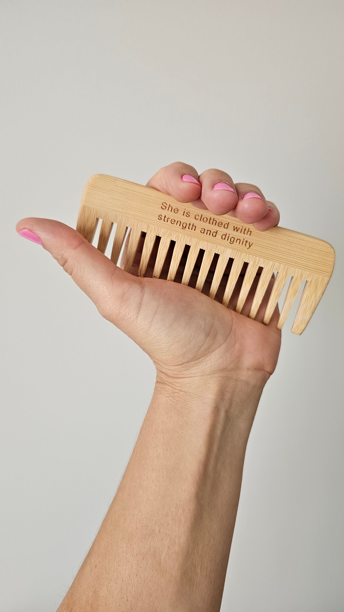 Hand holding a wooden comb with engraved text against a plain background